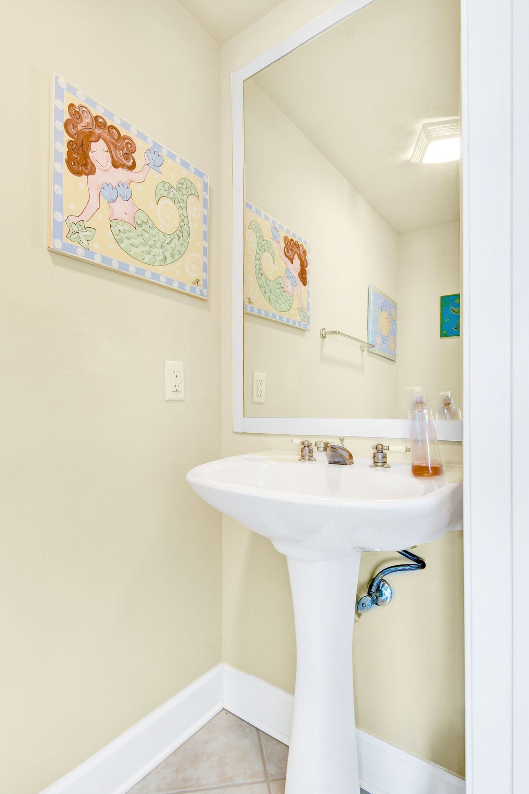 A bathroom with a white sink, a large mirror, and two wall-mounted artwork featuring mermaids.