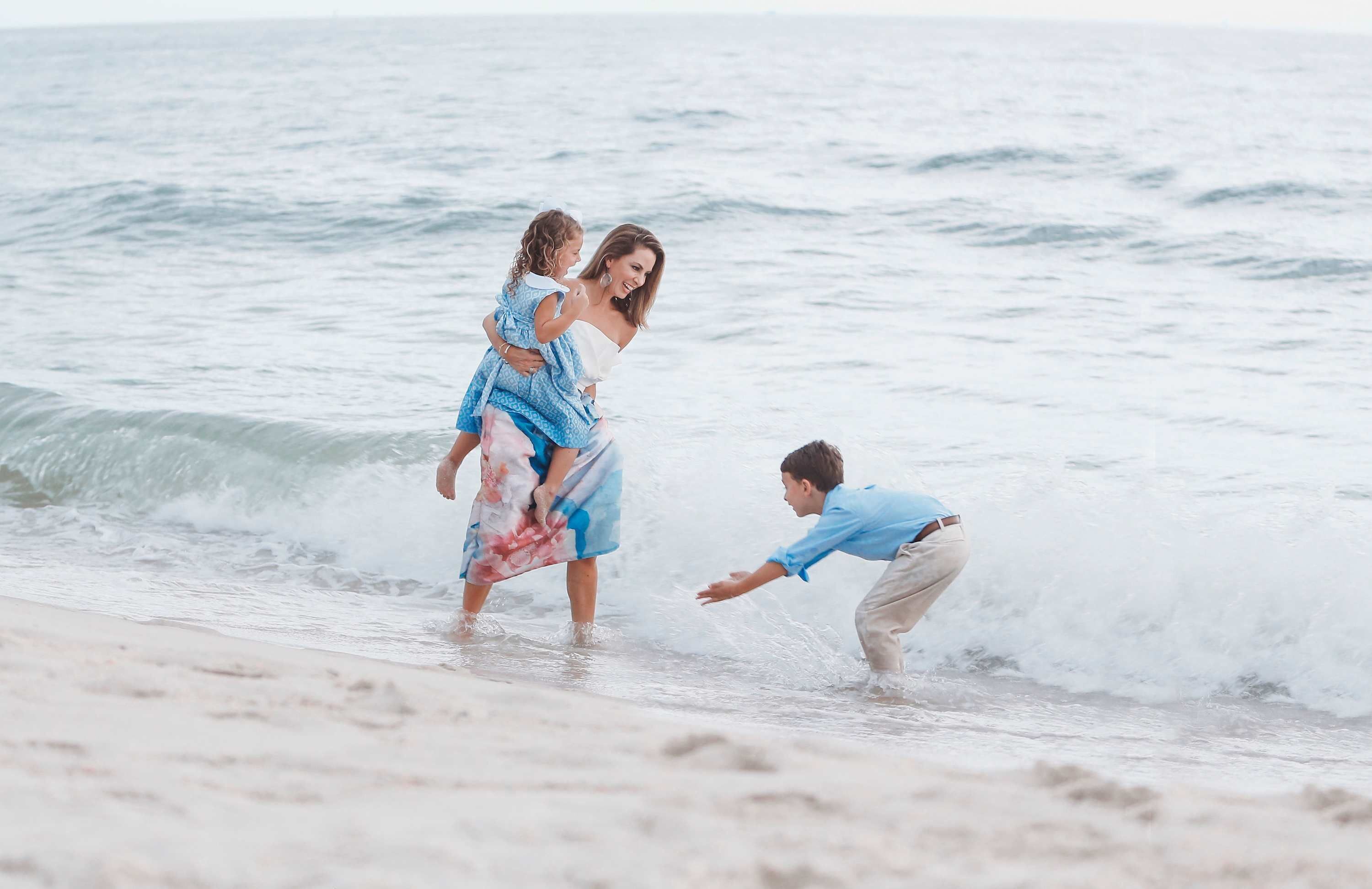 A beach scene with a person carrying a child on their back and another person in the water.