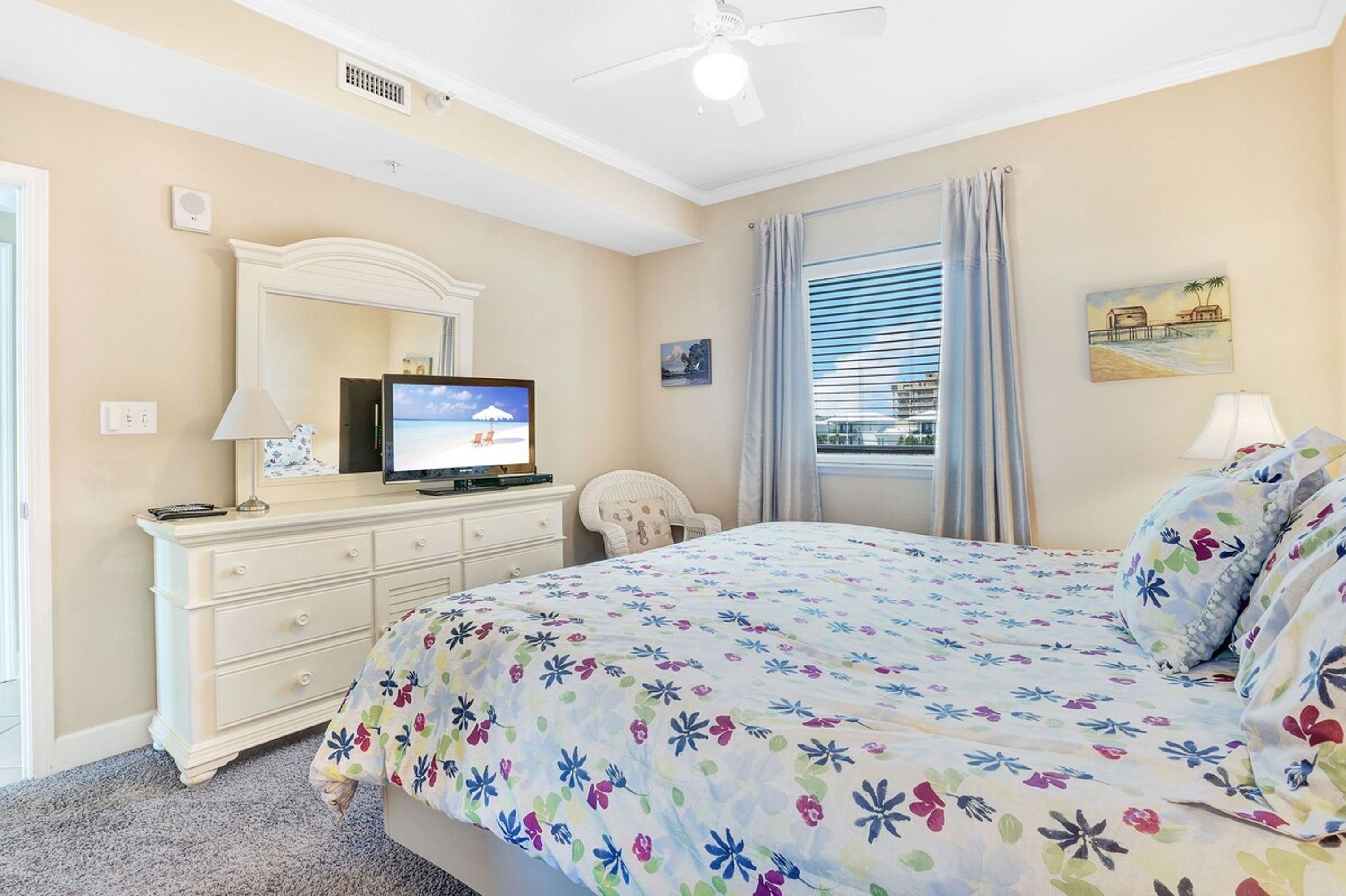 Ein Schlafzimmer mit Bett, Kommode, Fernseher, Stuhl und einem Fenster mit Vorhängen.