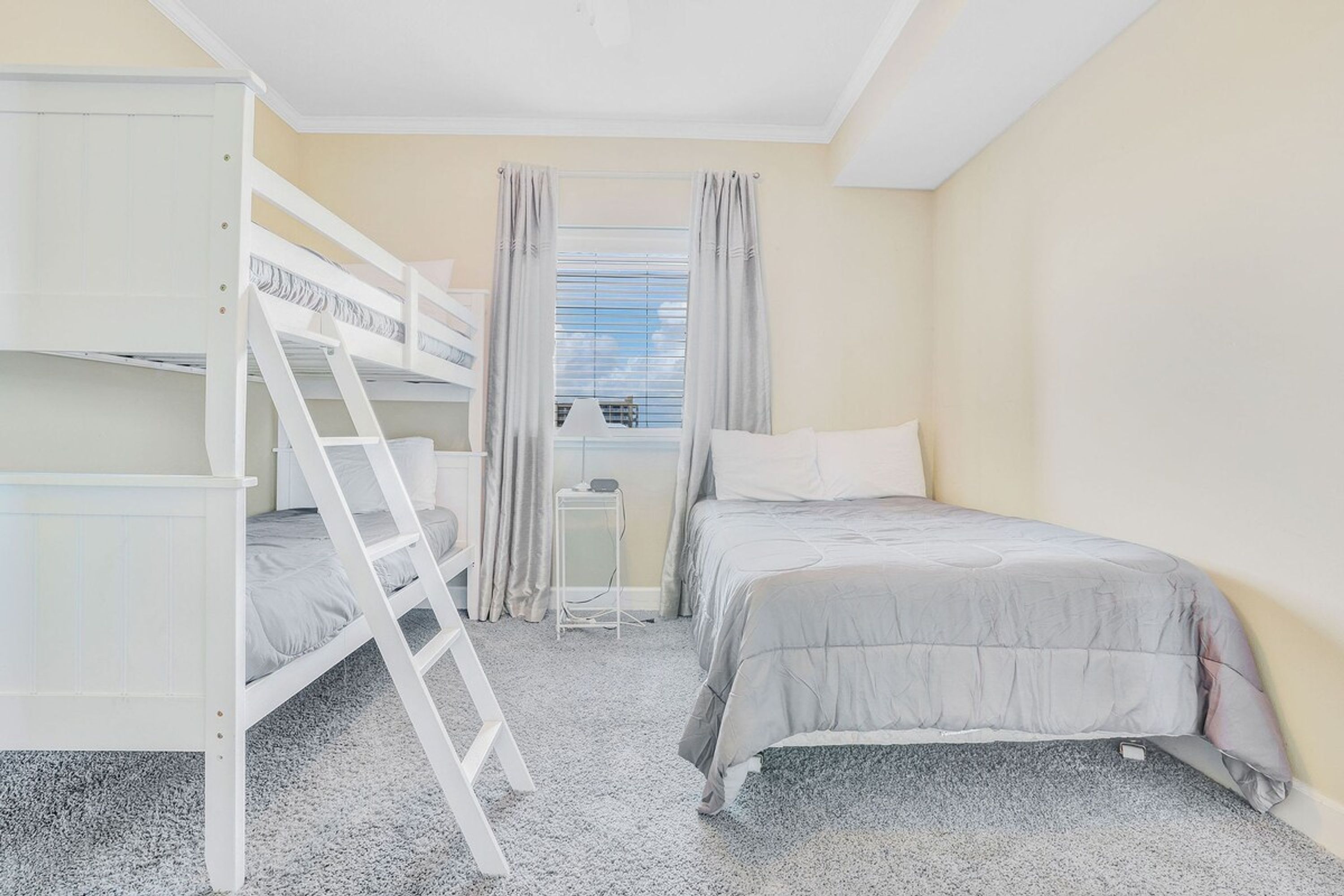 Een slaapkamer met stapelbedden, een ladder, een nachtkastje en een raam met gordijnen.