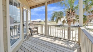 Ett trädäck med en stol, med utsikt över en strand med palmer och hus i bakgrunden.