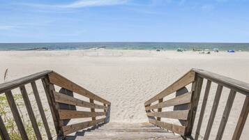 A wooden boardwalk leading to a sandy beach with a clear blue sky.