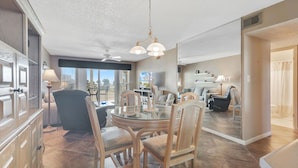 A spacious living area with a round glass table, wooden chairs, a ceiling fan, and a view of the outdoors. - Portside 108- On Ole River Bring Boat Pool (Orange Beach)