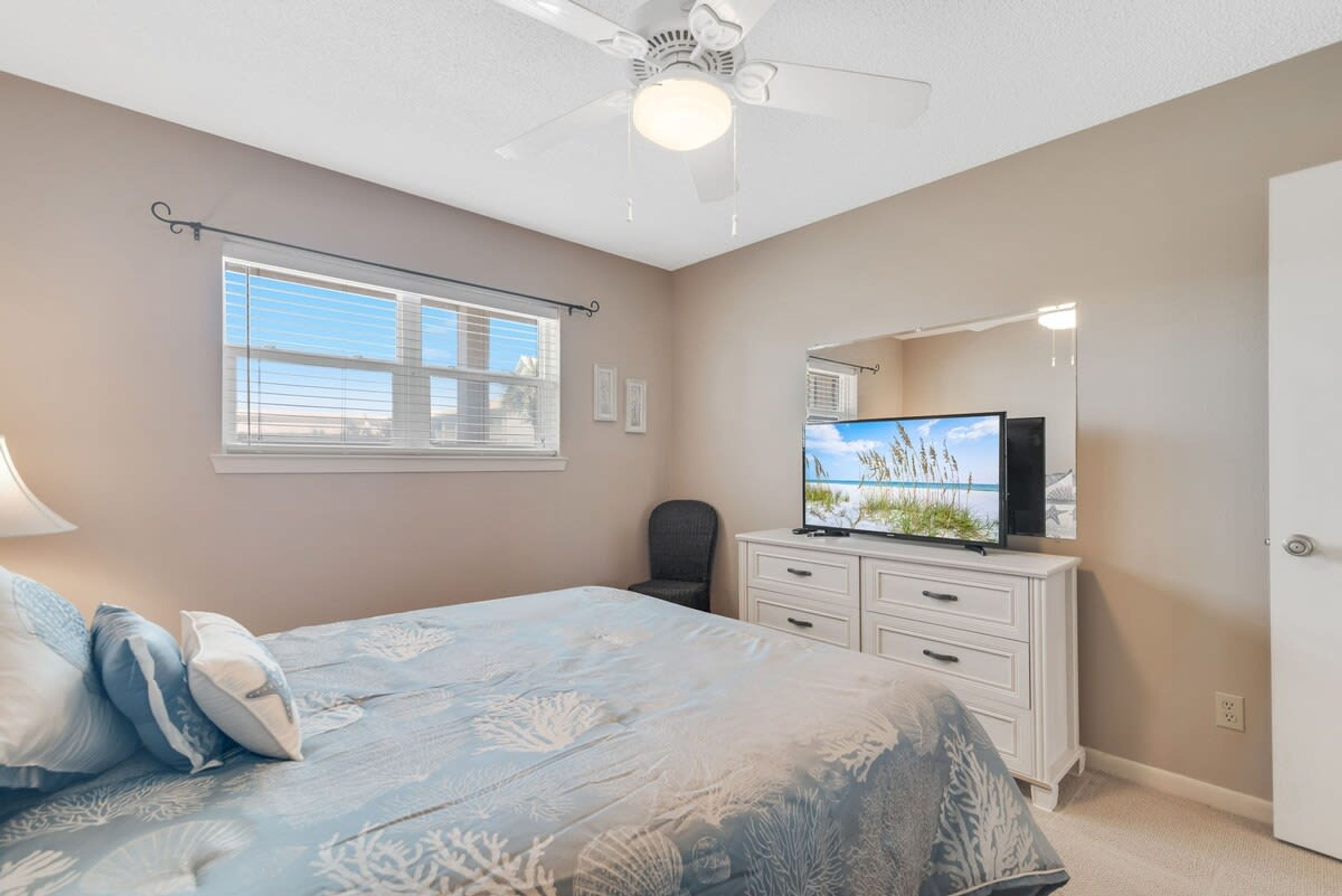 A bedroom with a bed, a ceiling fan, a TV, a dresser, and a window with blinds.