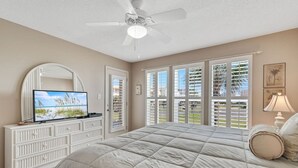 A bedroom with a large bed, a ceiling fan, a TV, and a view of the outside through the window. - Portside 108- On Ole River Bring Boat Pool (Orange Beach)