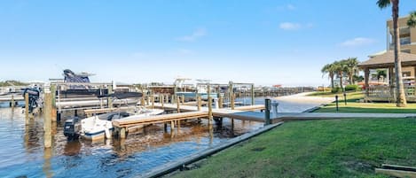 Un port de plaisance avec des bateaux amarrés, une zone herbeuse et un bâtiment orné d’un palmier.