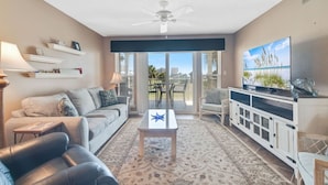 A living room with a sofa, coffee table, TV, and a balcony with outdoor furniture. - Portside 108- On Ole River Bring Boat Pool (Orange Beach)