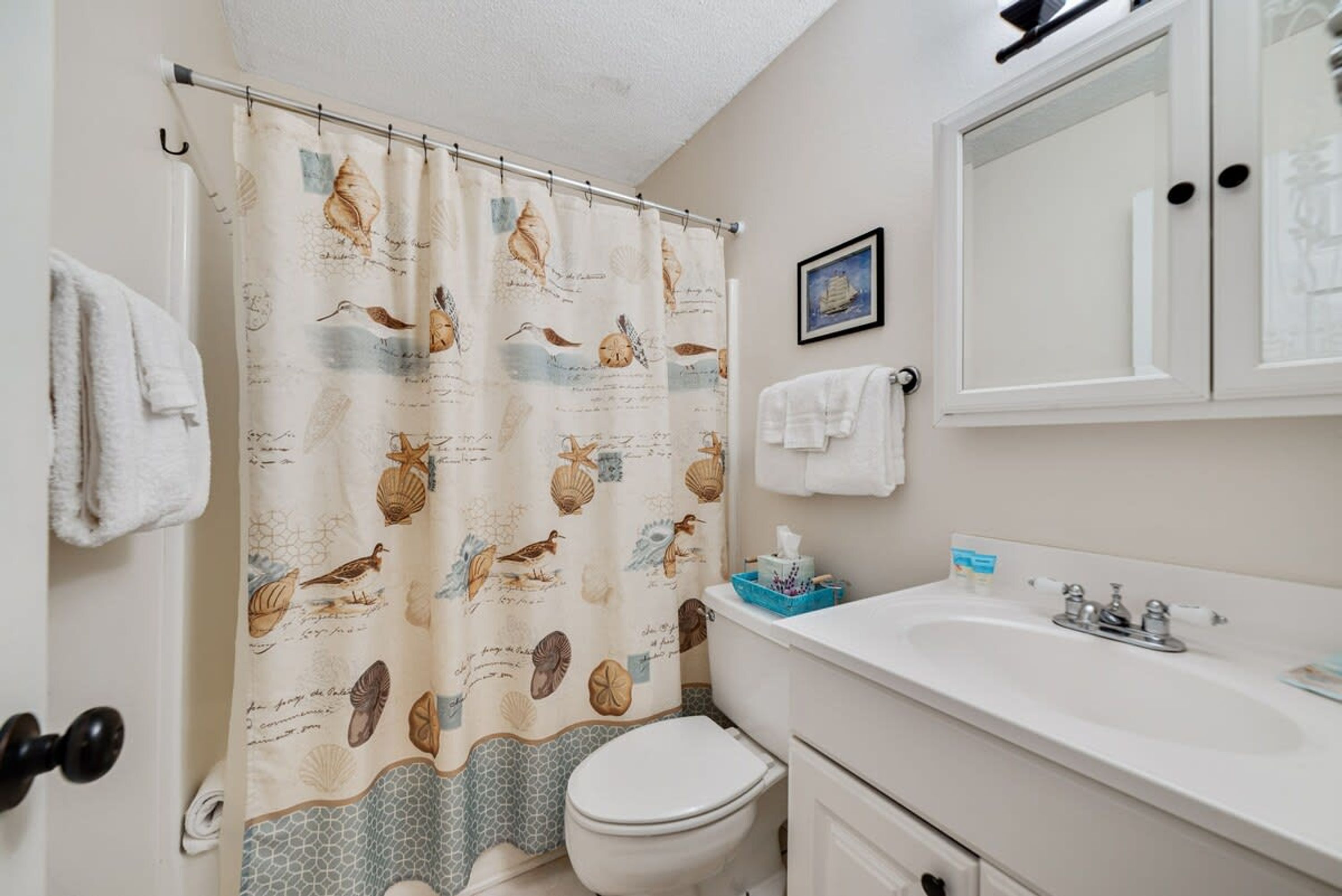 A bathroom with a shower curtain featuring sea creatures, a toilet, a sink, and a mirror.