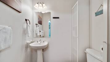Een badkamer met een wit wastafelmeubel, spiegel en toilet. Er is een handdoekrek met handdoeken en een bordje aan de muur.