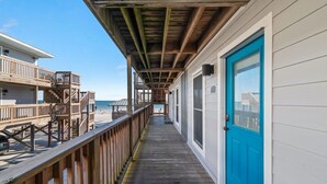 Een houten terras dat leidt naar een gebouw met een blauwe deur, een balkon en uitzicht op het strand.