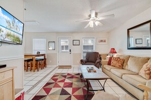 Ein Wohnzimmer mit Deckenventilator, einer Couch, einem Couchtisch und einem an der Wand befestigten Fernseher.