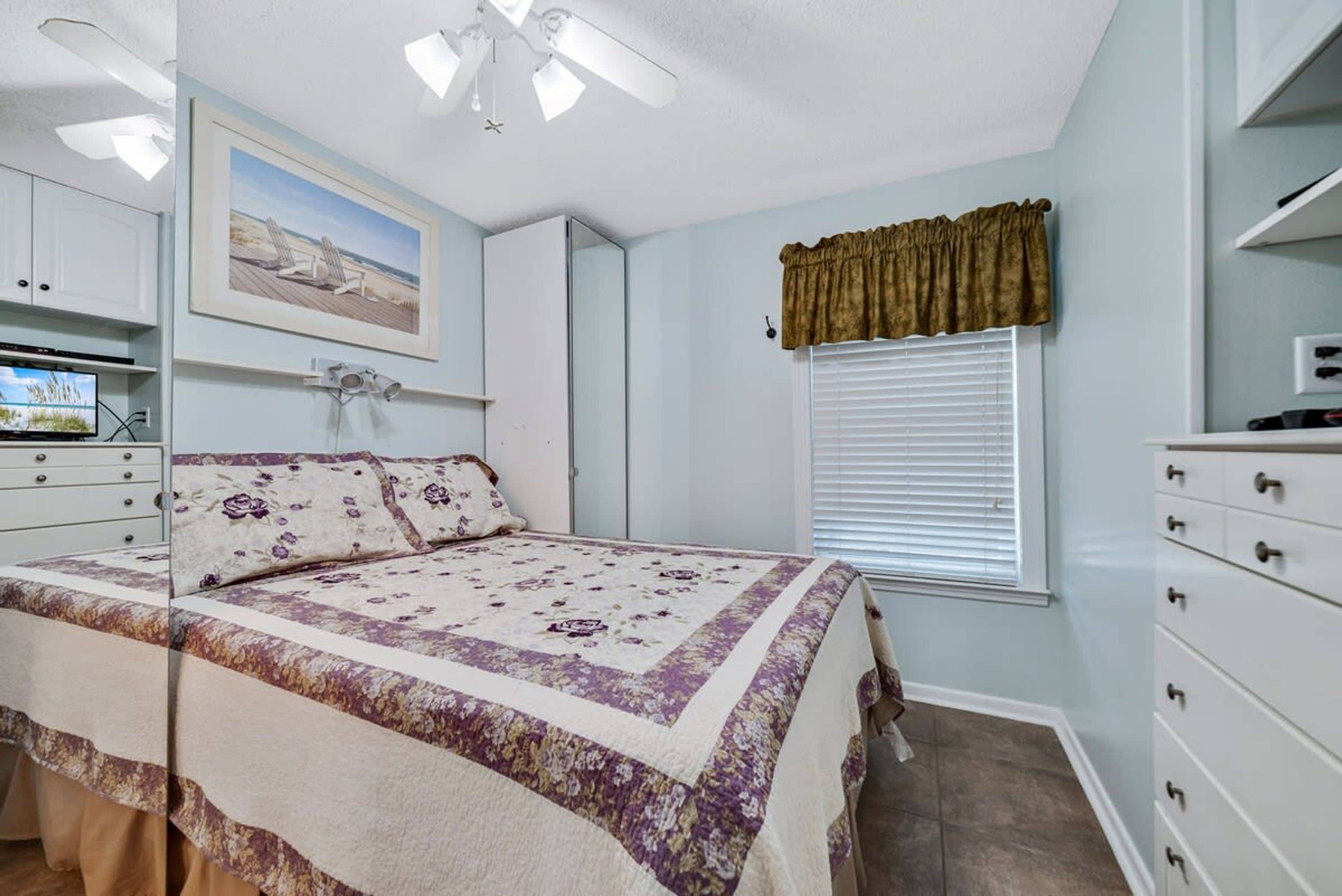 A bedroom with a bed, a ceiling fan, a window with blinds, and a painting on the wall.