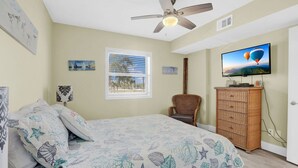 A bedroom with a bed, a ceiling fan, a television, a window with blinds, and a dresser. - Seaside Beach Racquet 4210- Beachfront Pools 2 Bedrooms 2 Baths (Orange Beach)