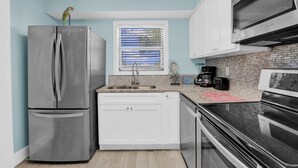 A modern kitchen with a stainless steel refrigerator, white cabinets, a brick backsplash, and a window with blinds. - Seaside Beach Racquet 4210- Beachfront Pools 2 Bedrooms 2 Baths (Orange Beach)