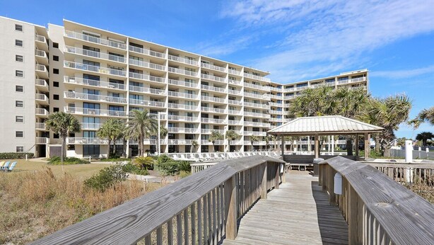 A wooden boardwalk leading to a multi-story hotel with balconies and a covered area. - Seaside Beach Racquet 4210- Beachfront Pools 2 Bedrooms 2 Baths (Orange Beach)