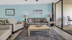 A living room with a ceiling fan, a sofa, a coffee table, and a painting on the wall. - Seaside Beach Racquet 4210- Beachfront Pools 2 Bedrooms 2 Baths (Orange Beach)