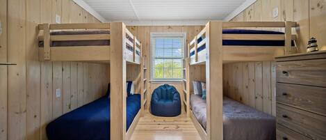 A compact room with bunk beds, a central bean bag chair, and a window with a view.