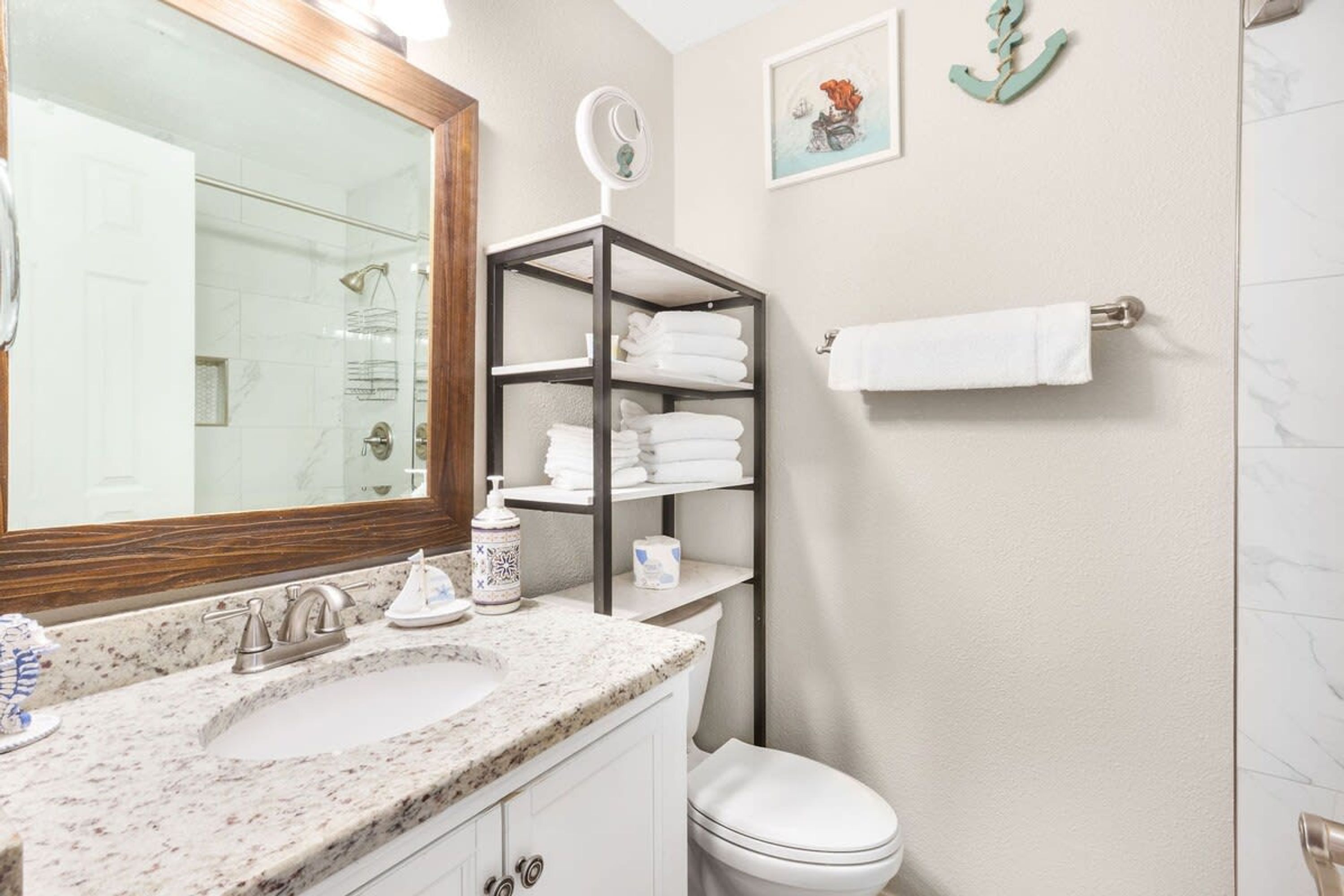 Un baño con un lavabo de mármol, inodoro, estante con toallas dobladas y espejo con marco de madera.