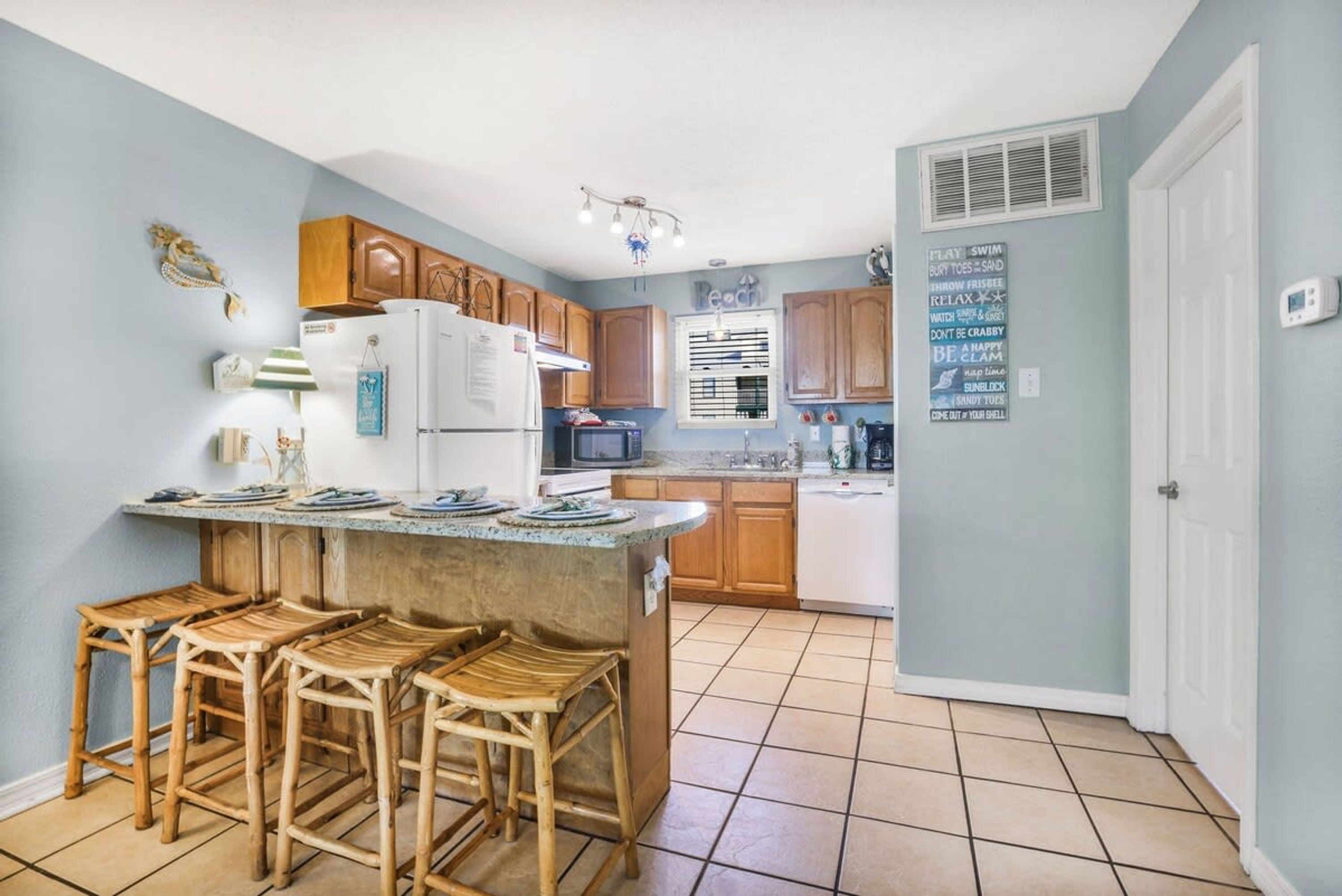 A kitchen with a central island, wooden bar stools, and a refrigerator.