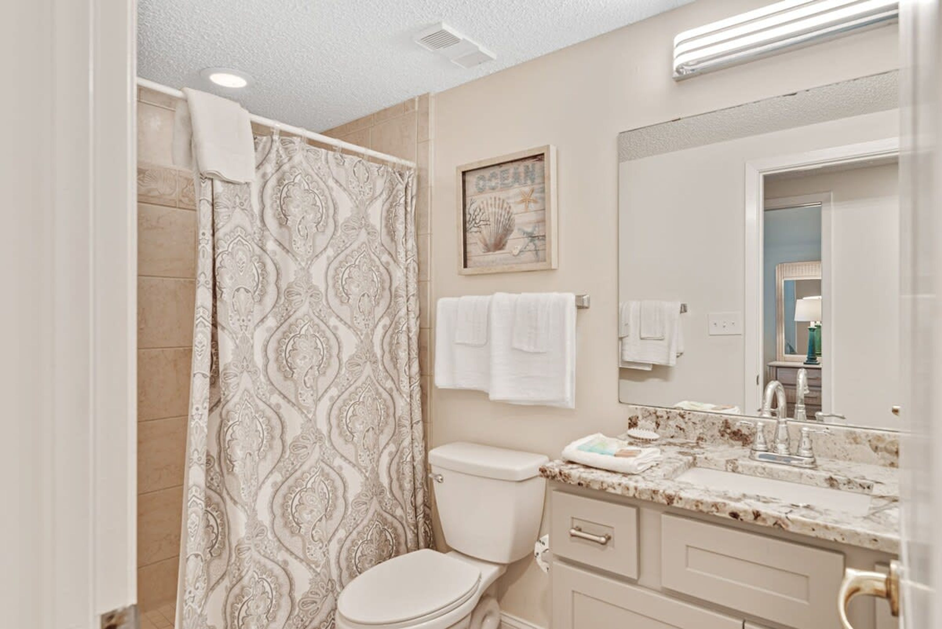 A bathroom with a patterned shower curtain, a toilet, a sink with a marble countertop, and a mirror.