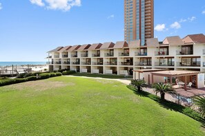 Ein Hotel mit mehreren Balkonen mit Blick auf einen Strand, einem Poolbereich und einem gepflegten Rasen.