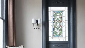 A room with a bench, a small table, a stained glass window, and a wall-mounted light fixture. - Historic Restoration, Whitefield Square (Savannah)