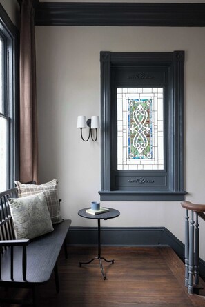 A room with a bench, a small table, a stained glass window, and a wall-mounted light fixture. - Historic Restoration | Whitefield Square (Savannah)