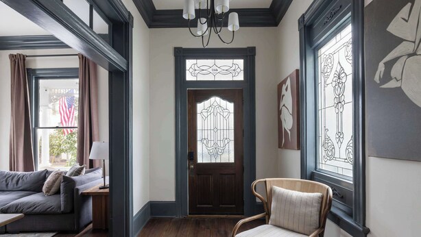 A room with a wooden floor, a sofa, a chair, a lamp, and a door with stained glass. - Historic Restoration, Whitefield Square (Savannah)