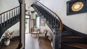 A grand staircase with a dark wooden finish and black balusters, leading to a room with a large stained glass window and a view of the outdoors. - Historic Restoration, Whitefield Square (Savannah)