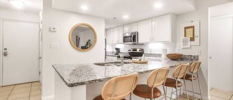 A modern kitchen with white cabinets, a granite countertop, a microwave, and a large island with bar stools.