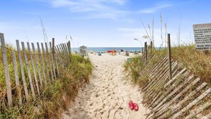 Un sentier de sable bordé de chaque côté par des clôtures en bois, qui mène à l’océan.