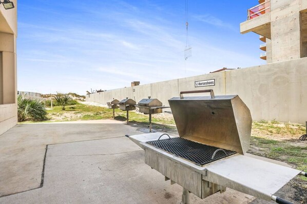 A barbecue grill with a metal grate, a concrete patio, and a building with a sign that reads "Horsehoes". - Sugar Beach153- 4 Pools Two Bedrooms 2 Baths Beach-side (Orange Beach)