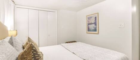 A bedroom with a bed, pillows, a wardrobe, and a painting on the wall.