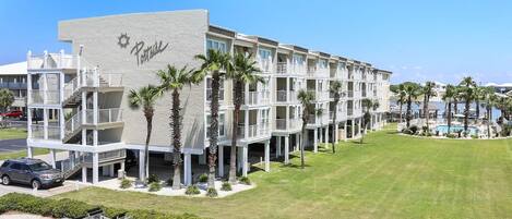A multi-story hotel with a pool area, palm trees, and a clear blue sky.