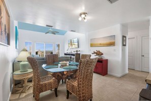 A dining area with wicker chairs and a glass-top table, a ceiling fan, and a city view through large windows. - Portside 304 Deeded Boat Slip w Lift Water View (Orange Beach)