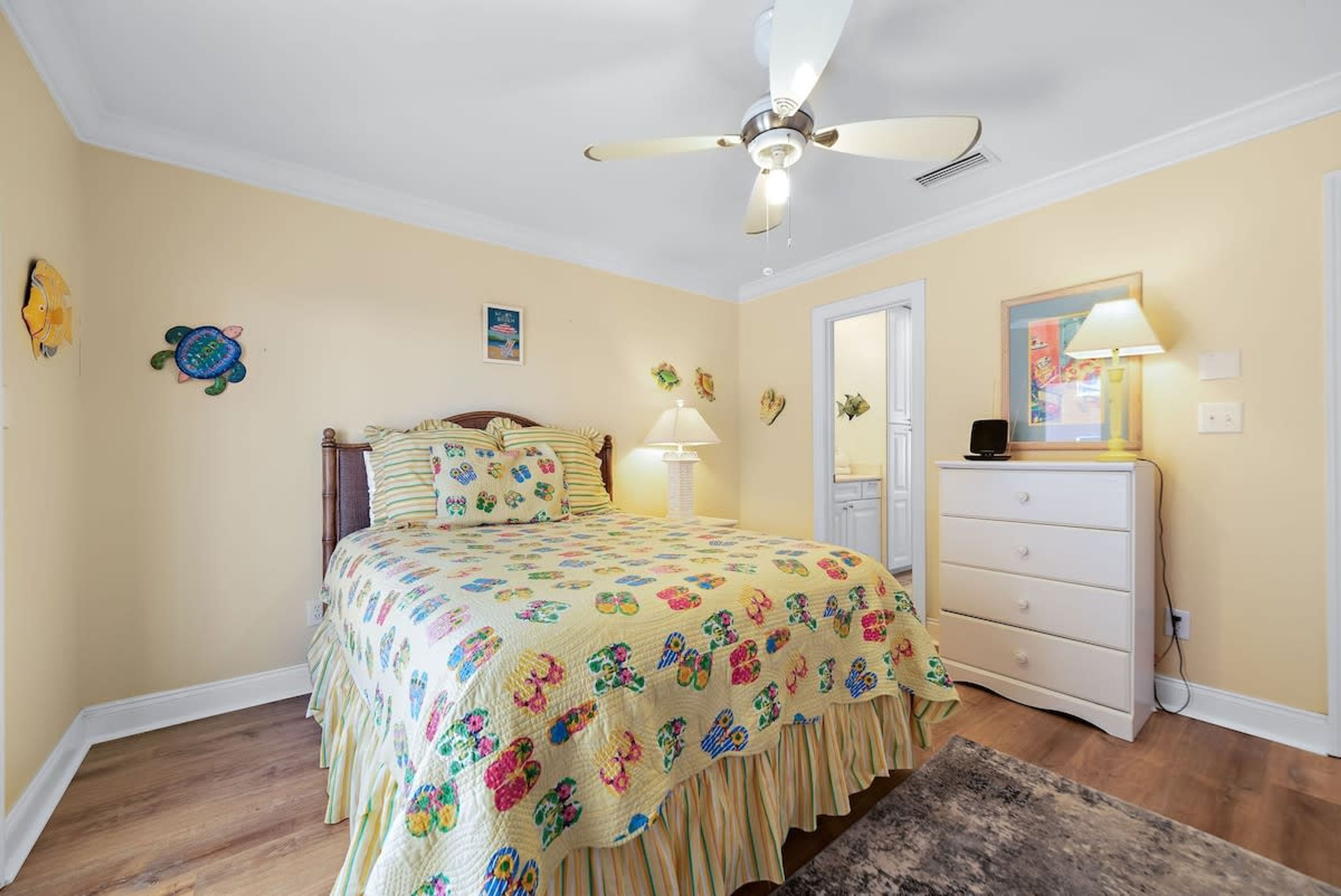 A bedroom with a bed, a dresser, a ceiling fan, and wall decorations.