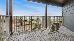 A balcony with a metal railing, a white chair, and a view of a residential area with houses and a road. - Sandpiper 1C- Stylish Gulf-side Affordable (Gulf Shores)