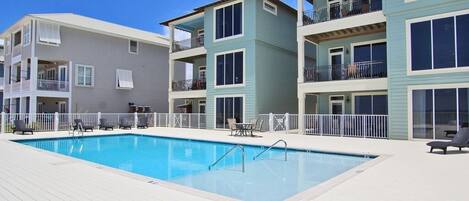 A swimming pool with a wooden deck, surrounded by multi-story buildings with balconies and railings.