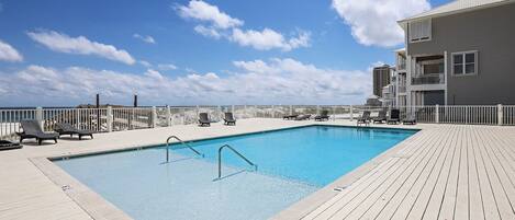 Una piscina rectangular con muelle de madera, sillas de descanso y cerca blanca.