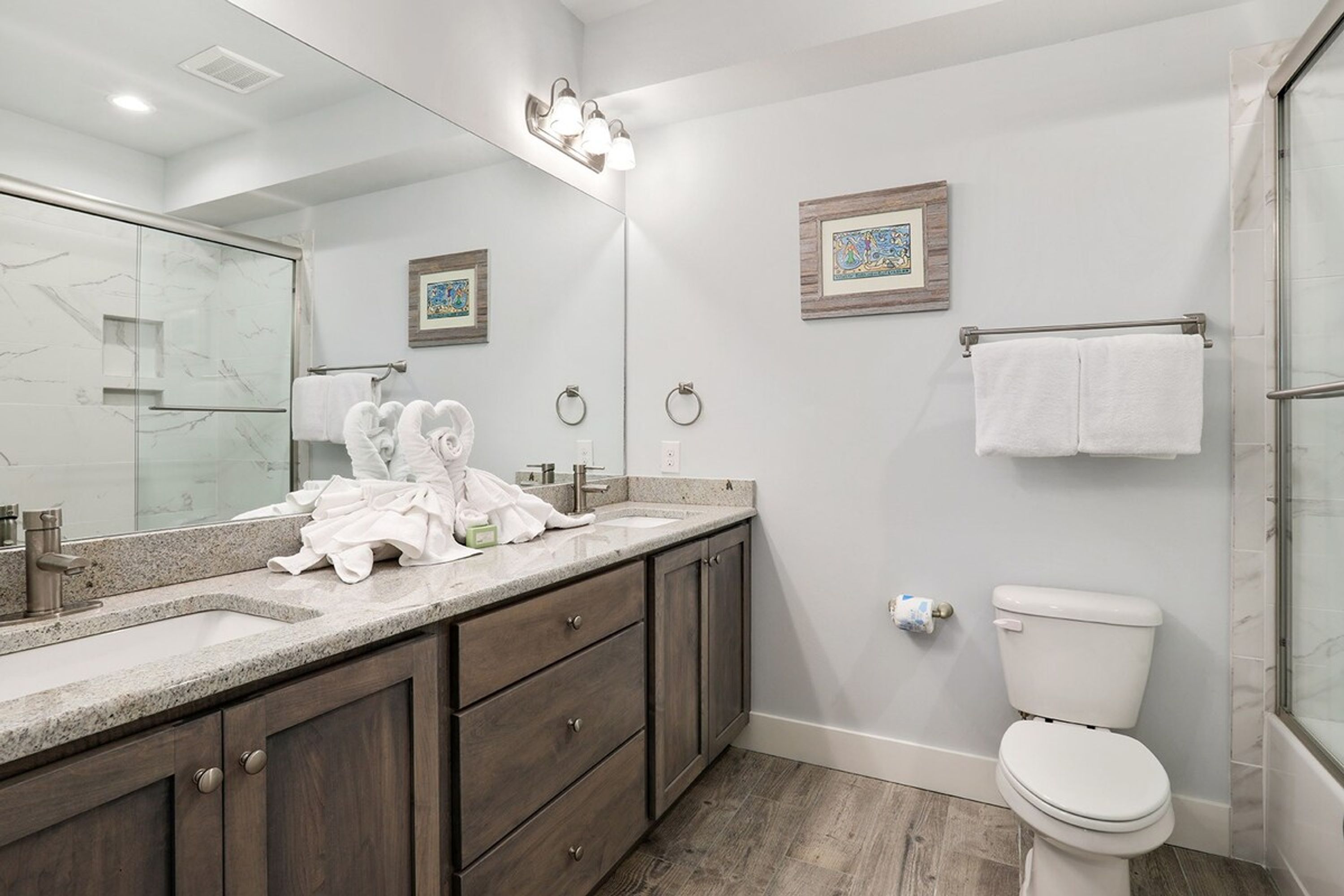 A modern bathroom with a large mirror, a granite countertop, wooden cabinets, a toilet, and a shower area.