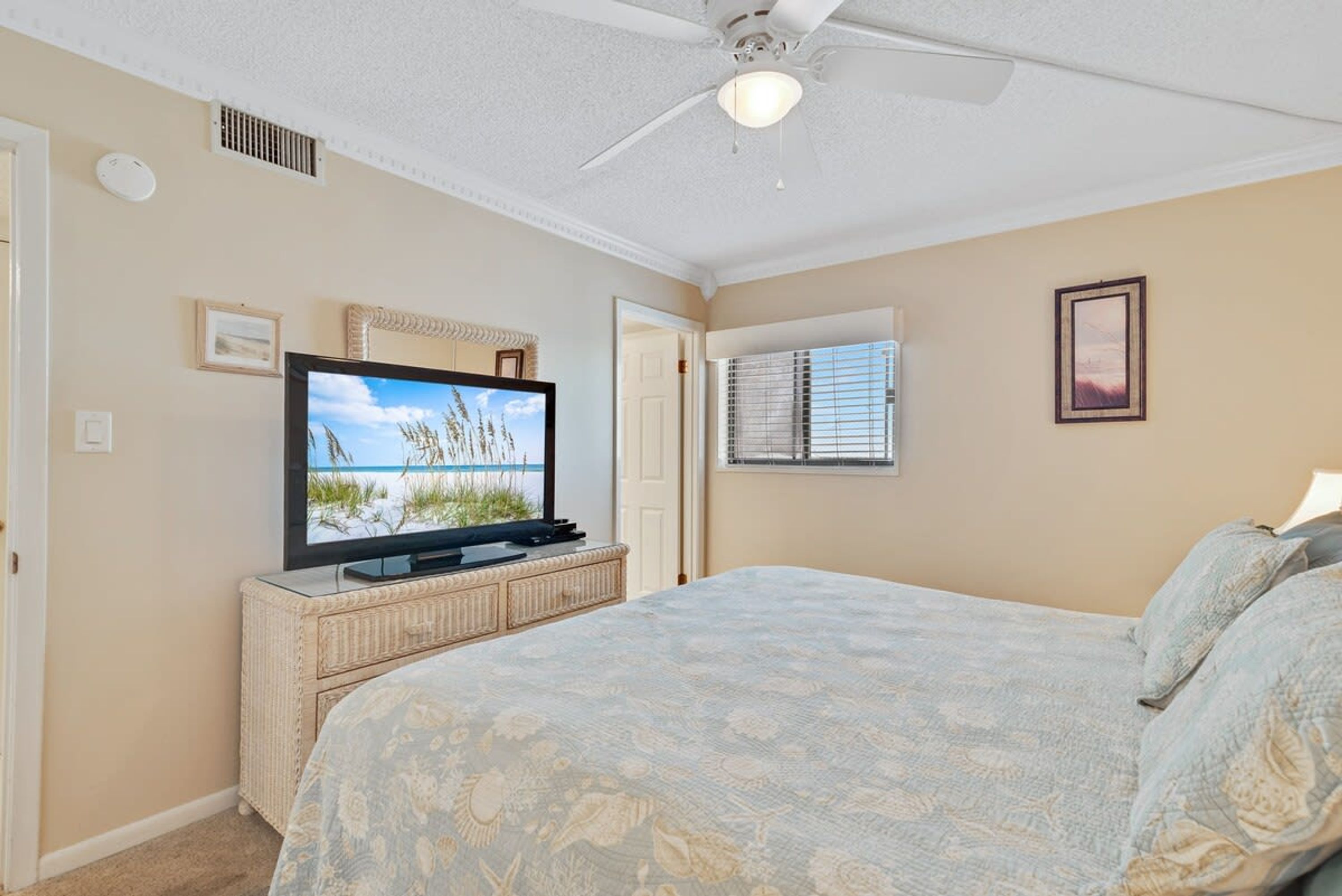 A bedroom with a bed, a television on a cabinet, a ceiling fan, and a window with blinds.