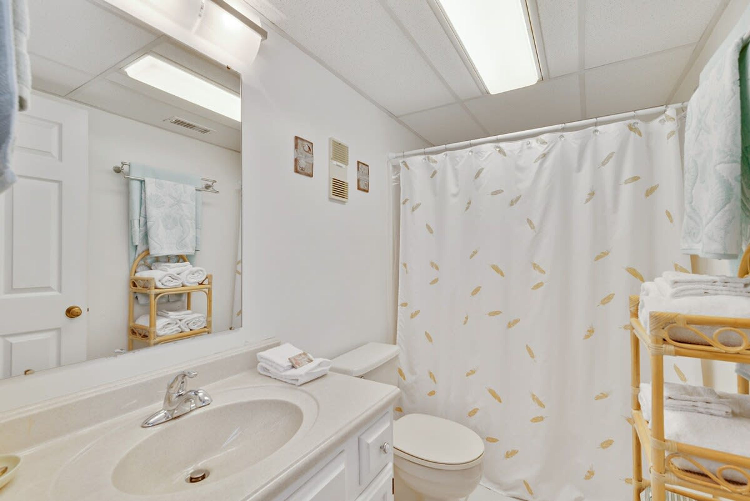 A bathroom with a white sink, mirror, and toilet. There is a shower curtain with a leaf pattern.