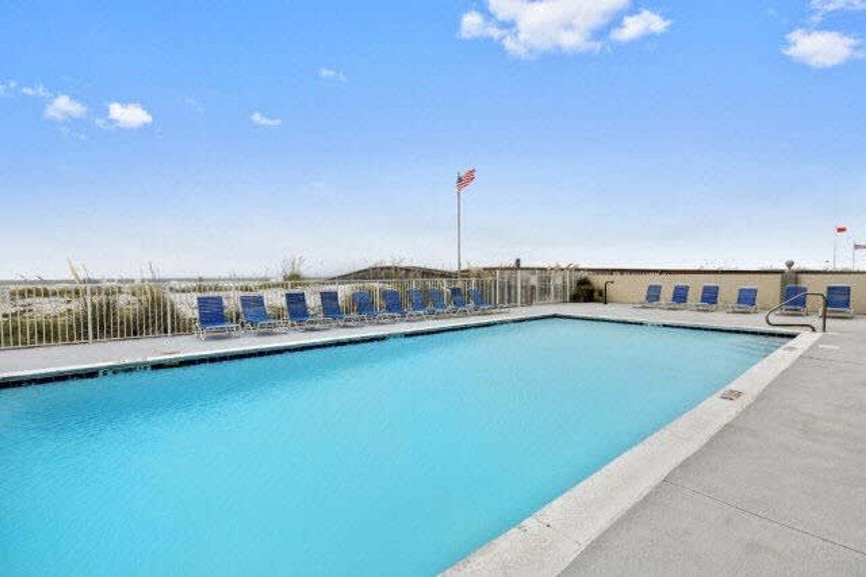 A swimming pool with blue chairs and a flagpole with an American flag.
