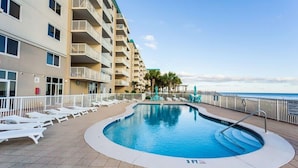 Una piscina con sillas de descanso, un edificio con balcones y vista al océano.