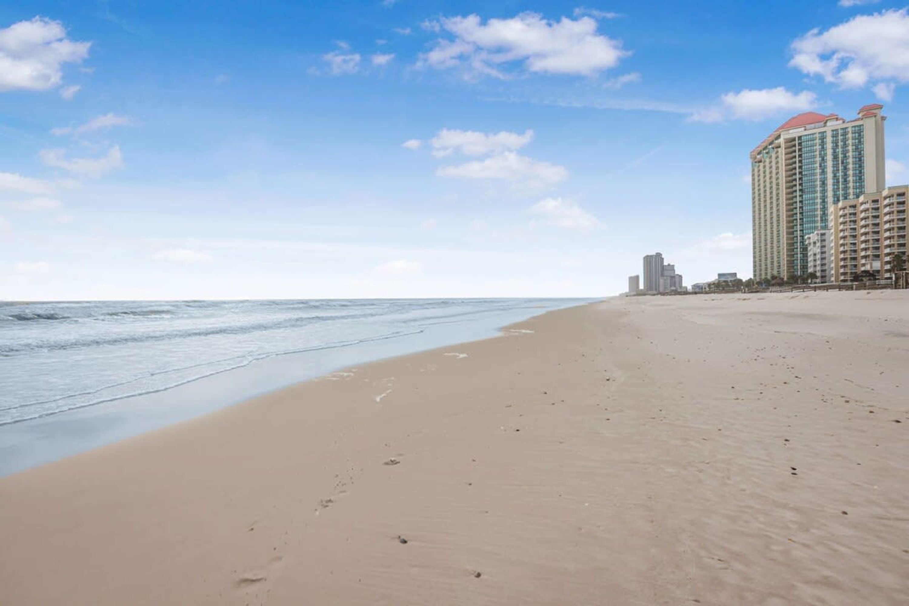 A beach with a clear sky and a large hotel building with a red roof in the background.