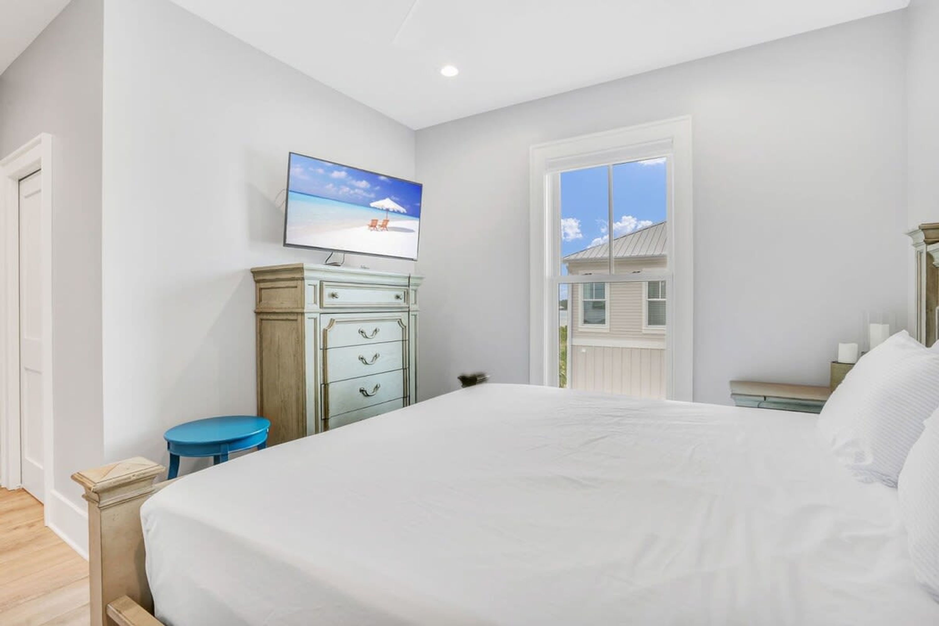 Une chambre à coucher avec un grand lit, une commode, un téléviseur et une fenêtre donnant sur une maison.