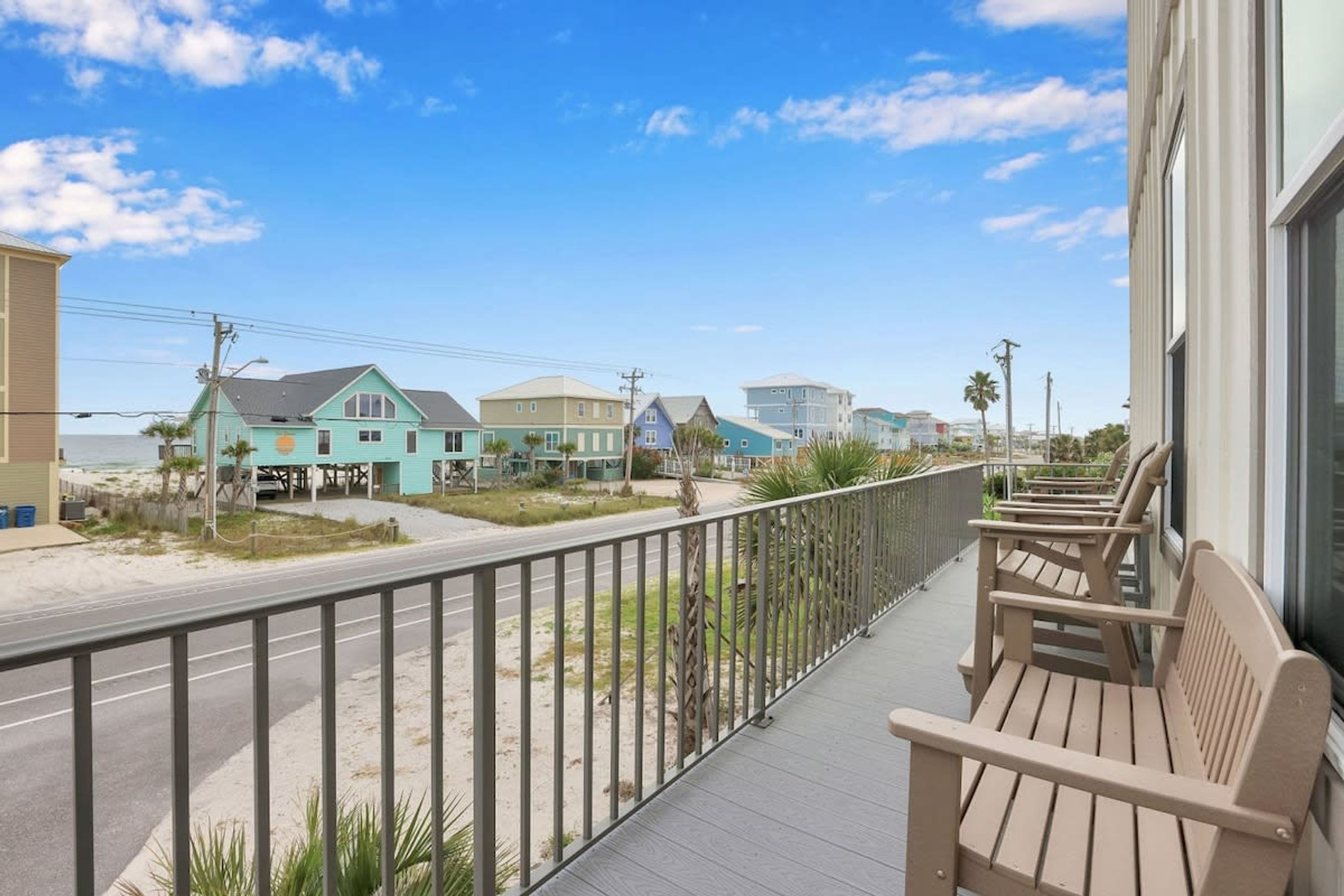 A balcony with wooden chairs, a view of a beach, and houses in the background.