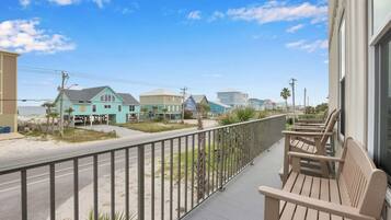 A balcony with wooden chairs, a view of a beach, and houses in the background.