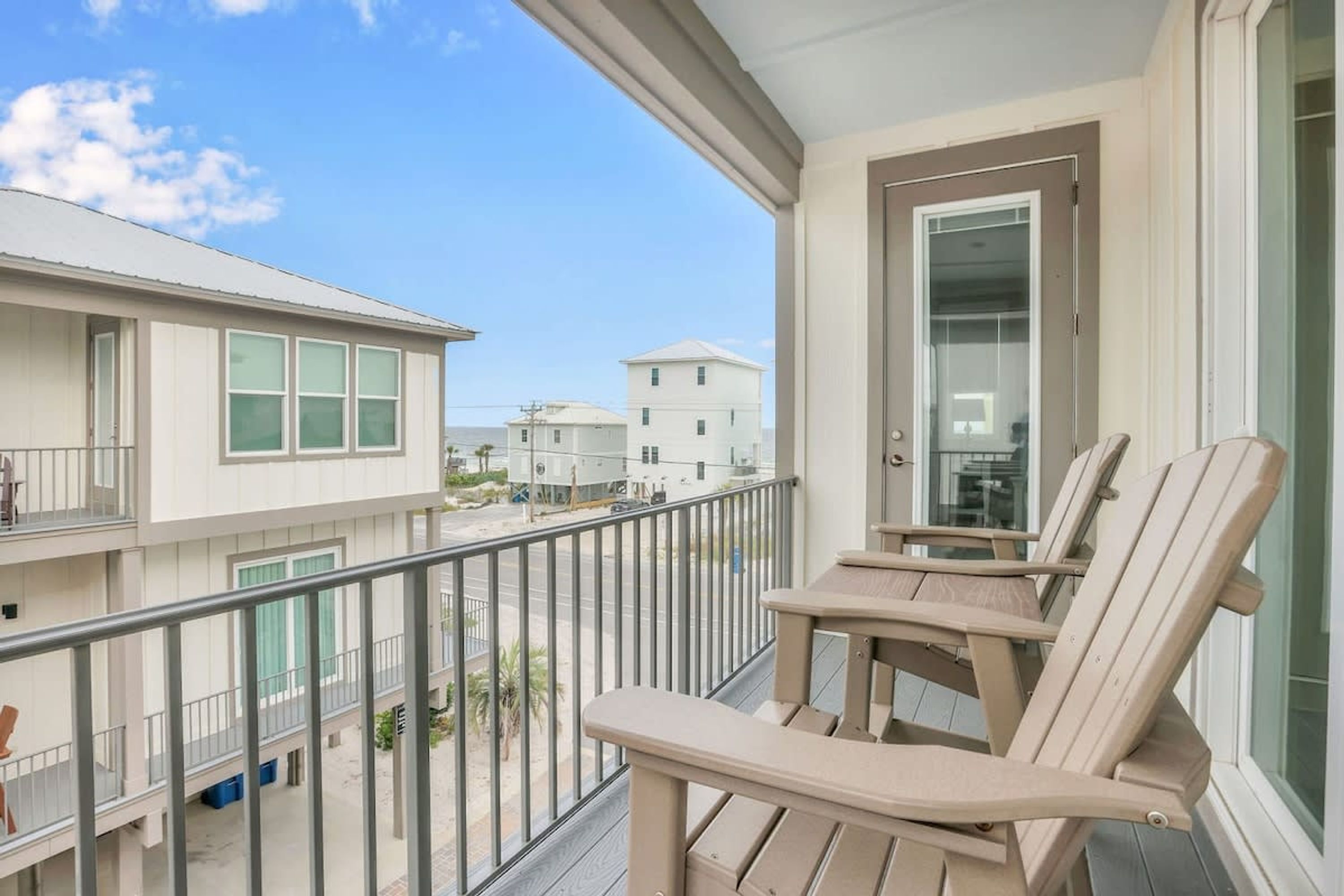 A balcony with two Adirondack chairs, a glass door, and a view of neighboring buildings.