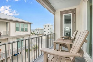 A balcony with two chairs, a railing, and a view of neighboring buildings. - Life s Porpoise A Steps From Beach Pool (Gulf Shores)